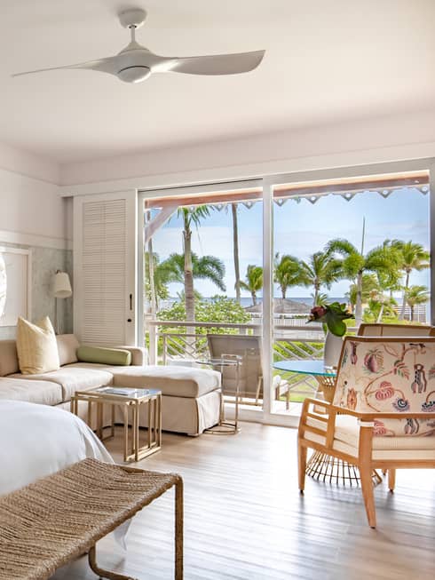 Light and airy luxury resort room with king bed, sitting area with a sofa and arm chair, and walk-out terrace to tropical setting