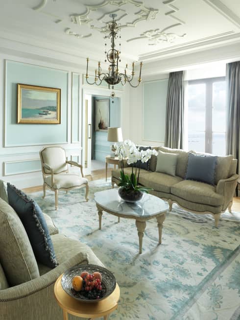 Presidential Suite sunny living room with two elegant sofas, coffee table under small chandelier by window, marble fireplace