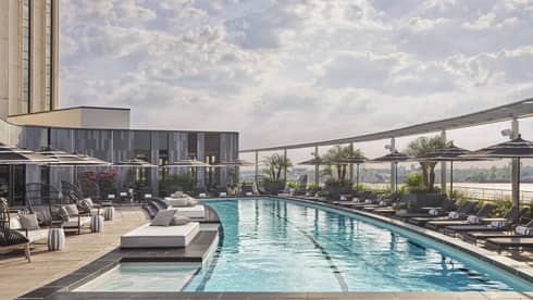 A slightly curved outdoor lap pool with lounge chairs and umbrellas along both sides