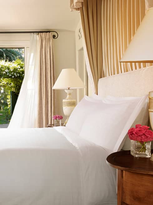 Bungalow Room side of bed with white linens, desk under large gold-framed mirror by open patio door