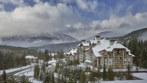 An external shot of FS Whistler covered in snow, with a large mountain behind. 