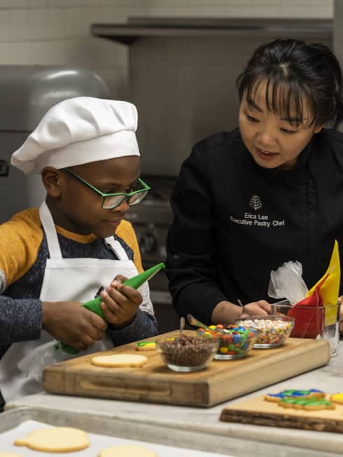 Two young children decorate cookies with the help of a chef
