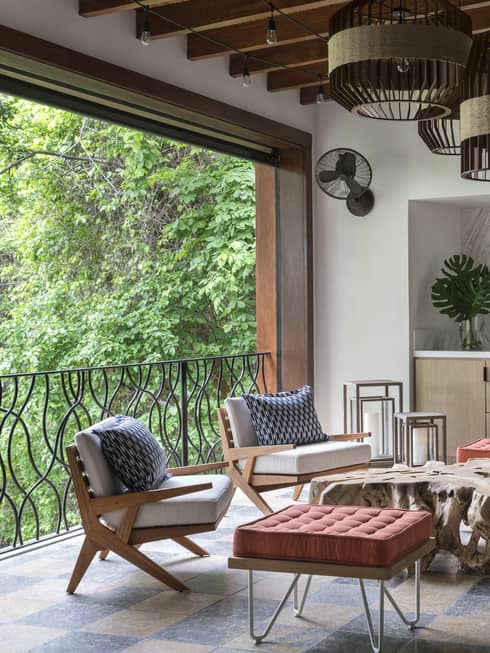 Modern cushioned armchairs, large tufted footstools beside open wall with iron terrace