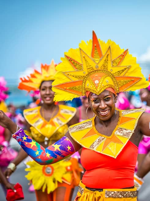 Women in brightly colored outfits with headdresses and arm bands smile and dance