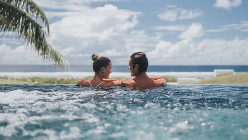Back of couple at edge of whirlpool overlooking ocean, blue sky 