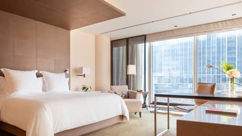 Guest room with large windows, city views, king bed, lamp, armchair and workspace