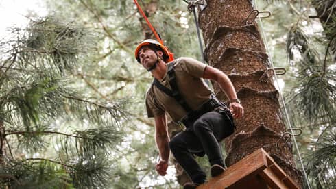 Man wearing harness and helmet prepares to leap from platform in tree