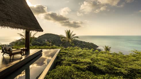 Patio lounge chair, thatched roof and deck overlooking canopy of tropical trees, ocean