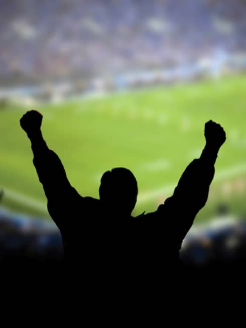 A silhouette of a person cheering at a football stadium.