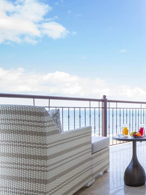 Modern wicker armchair, ottoman by table with breakfast, fresh juice on balcony overlooking sea
