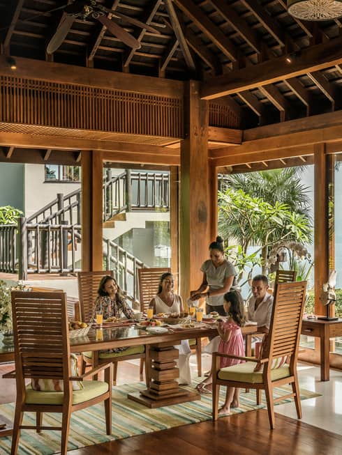 Butler serves family at long table in bright corner window dining room with windows
