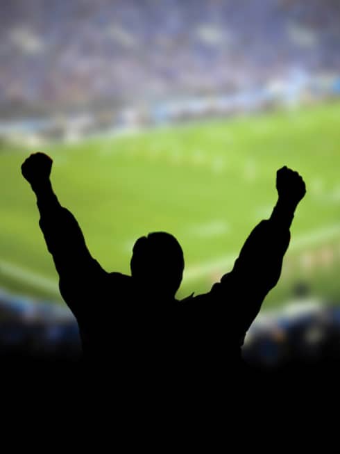 A silhouette of a person cheering at a football stadium.