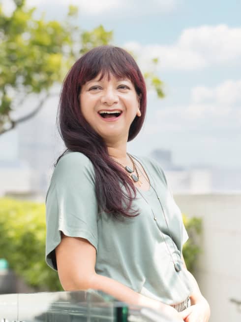 A smiling resident healer Cheryl Rodriguez poses outdoors, downtown Hong Kong looming behind her