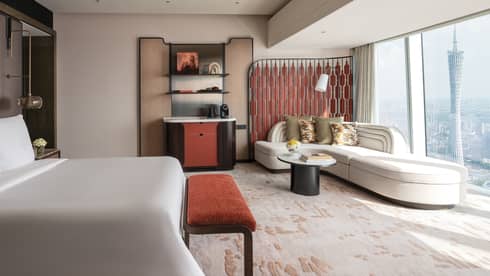 Sleek hotel room with king bed, sofa, wet bar and wall of windows with view of iconic city tower