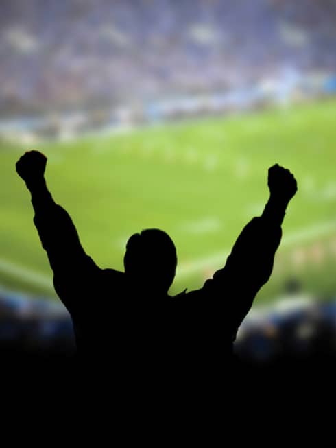 A silhouette of a person cheering at a football stadium.
