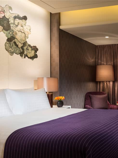 Hotel room bed with purple blanket under black-and-white Chinese brushwork mural