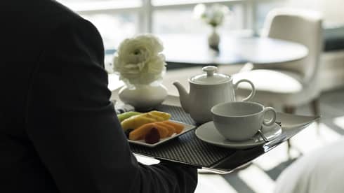 A man carries a tray of tea inside a hotel guest room with window