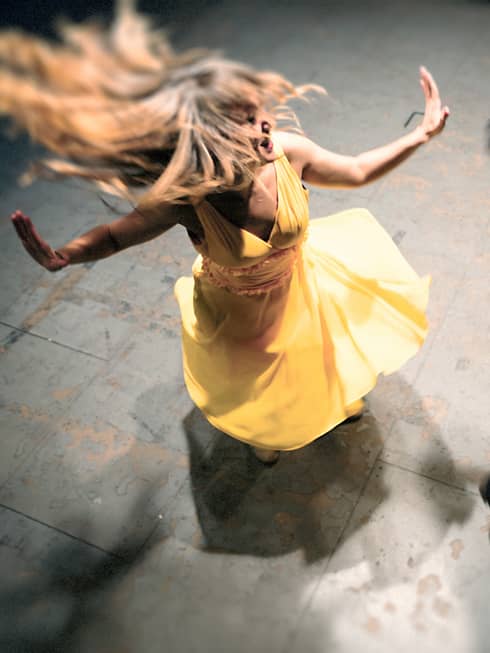 Woman in a yellow dress is spinning on the dance floor as a man wearing all black dances next to her