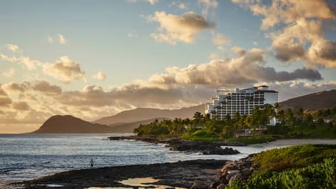 Sunset over Four Seasons Resort Oahu building on rugged coast, Waianae mountains