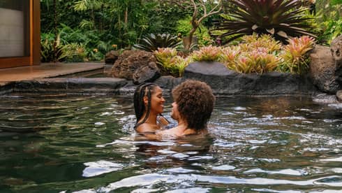 A man and woman embrace in a pond-like pool at a tropical resort