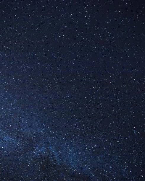 Thousands of stars dusting across a clear night sky; a cluster of stars form the Milky Way, just barely visible in the sky.