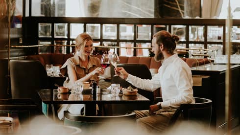 Smiling couple at table toasts with wine glasses in restaurant lounge 