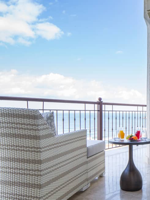 Modern wicker armchair, ottoman by table with breakfast, fresh juice on balcony overlooking sea
