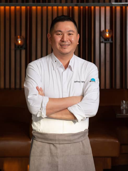 An asian chef in a grey apron.