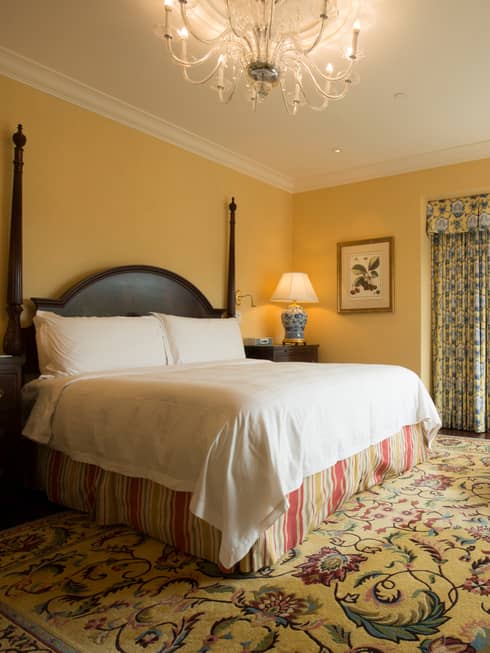 Malibu Corner One-bedroom Suite poster bed with striped skirt under chandelier