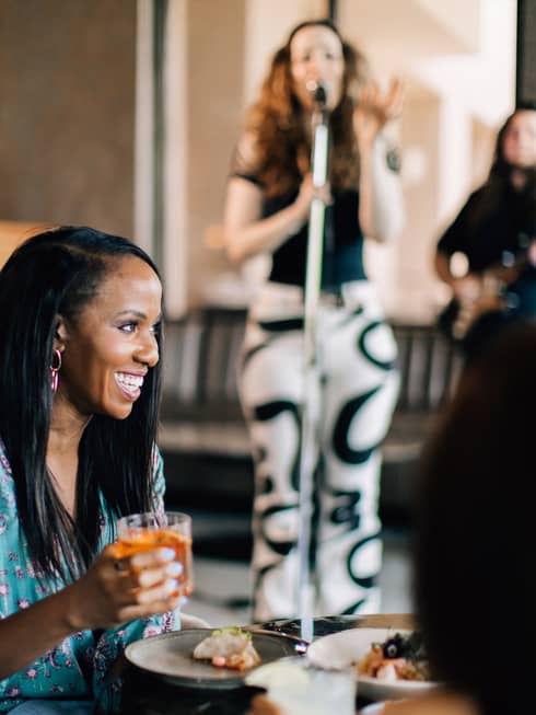 A woman singing in the background while people are eating and talking.
