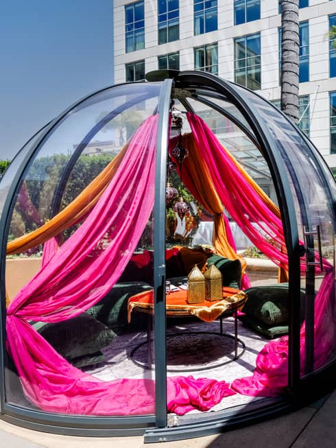 A dining table and chairs inside of a glass dome with buildings and the sky in the background