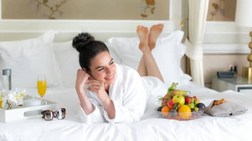A woman in a spa robe laying on a bed with juice and fruit.