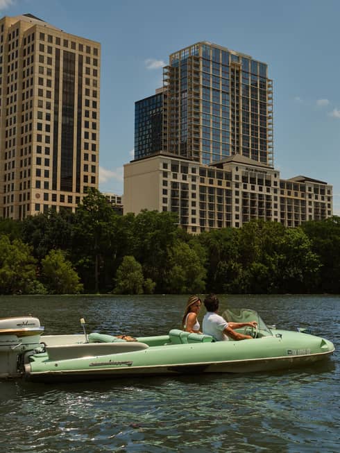 Two guests on a boat in the water with city buildings in the background