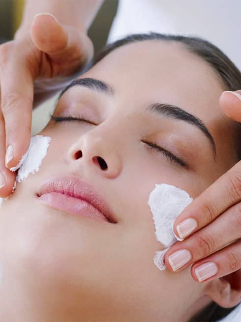 Woman closes eyes as spa staff rubs cream on cheeks