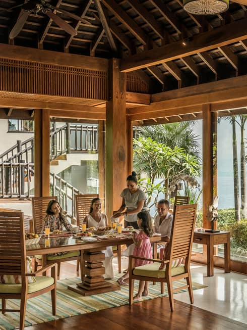 Butler serves family at long table in bright corner window dining room with windows