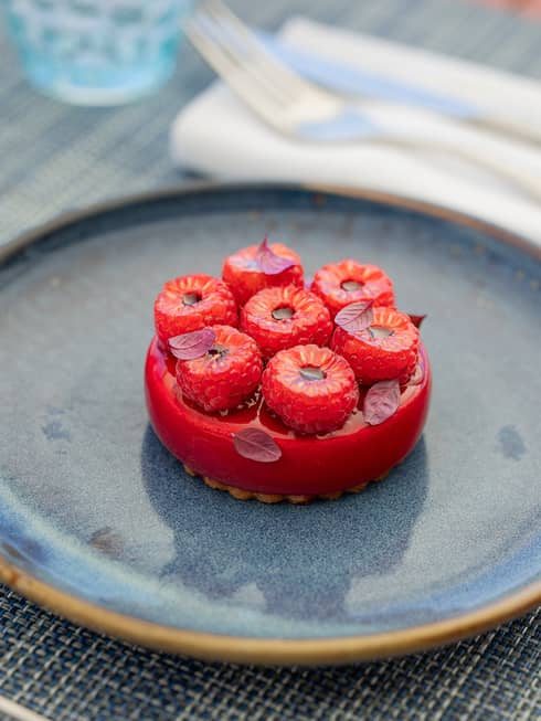 Round raspberry-glazed dessert topped with fresh raspberries on blue ceramic plate