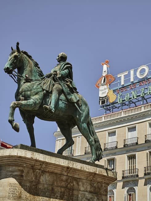 A statue of King Charles III of Spain on horseback in front of the Tio Pepe neon sign. The sign is on a sunny roof.