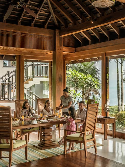 Butler serves family at long table in bright corner window dining room with windows