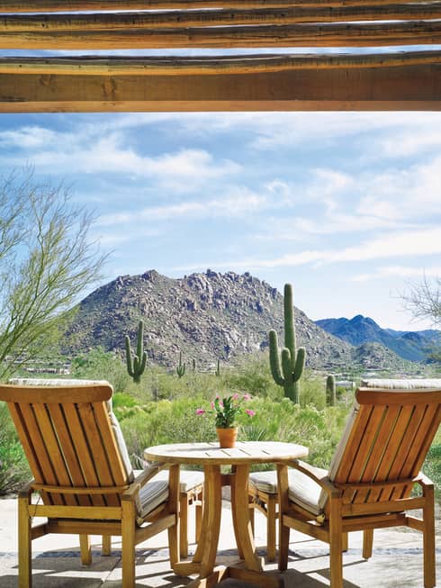 Back of two wood armchairs, table facing desert, cactus