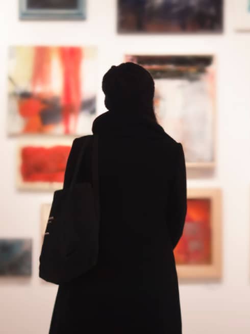 Silhouette of back of woman with hat bag looking at gallery wall with colourful art
