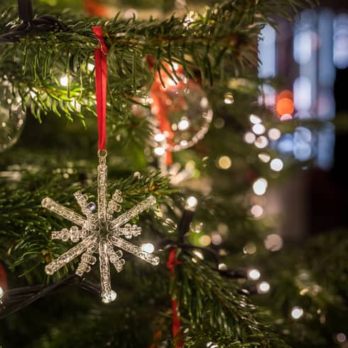 Close-up of a crystal snowflake ornament hanging on a Christmas tree with festive lights in the background