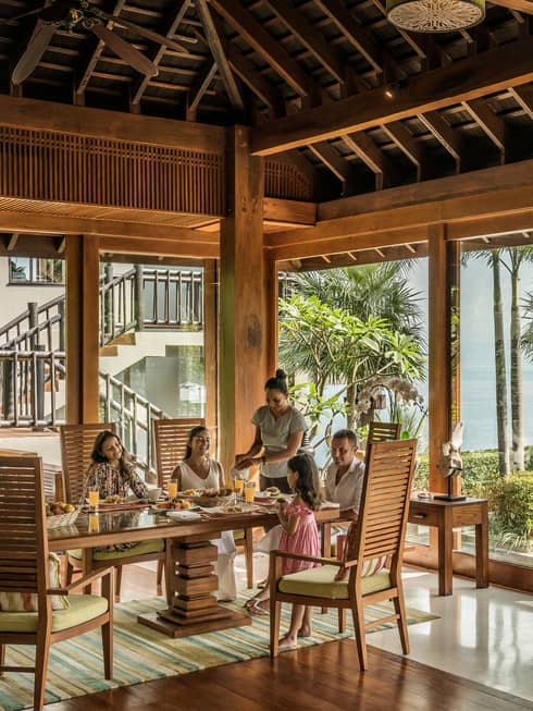 Butler serves family at long table in bright corner window dining room with windows