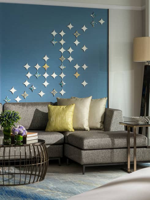 Gold pillows on grey sofa against blue wall with star-shaped Peranakan tile mural