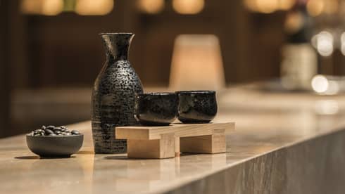 Close-up of black sake jug with two cups on wood tray on marble bar
