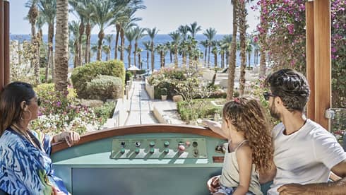 Woman, little girl and man look at view of palm trees and Red Sea from funicular car at Four Seasons Resort Sharm El Sheikh