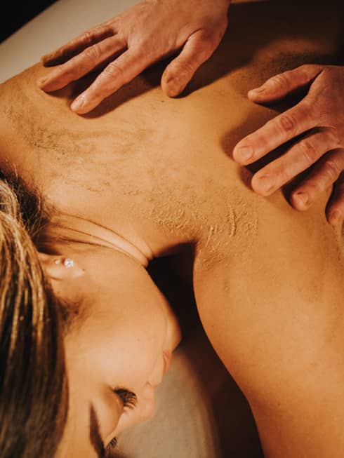 Two hands on woman's bare back as she lays on massage table in dimly lit room