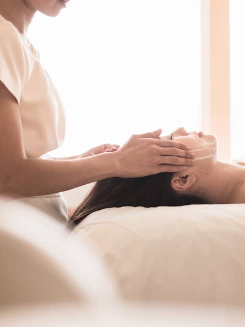 Spa staff massages woman's forehead, temples as she lies on massage table