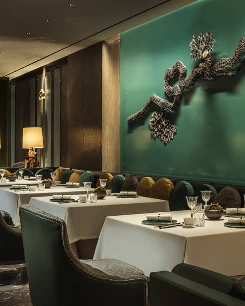 Yu Yuan dining tables, chairs under green wall with modern wire sculpture