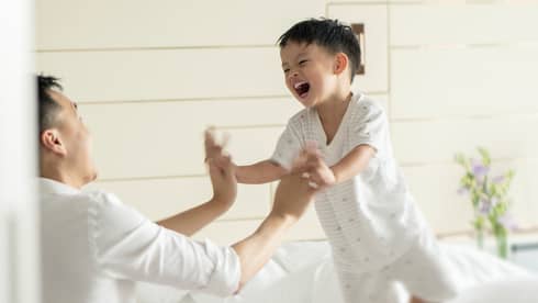 Man and young boy in white pyjamas laugh, jump on bed