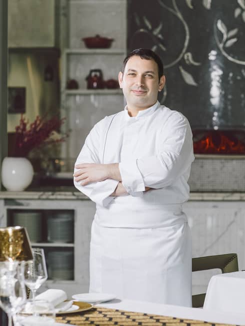 Portrait photo of Executive Sous Chef Luca Casini in white uniform, standing at white table
